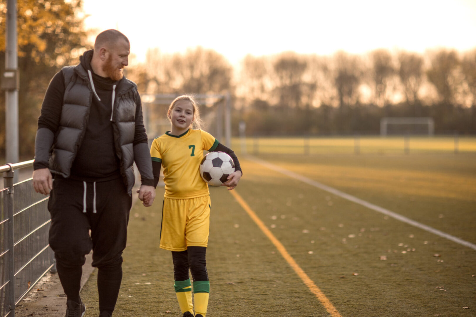 Father and daughter walking on soccer field.