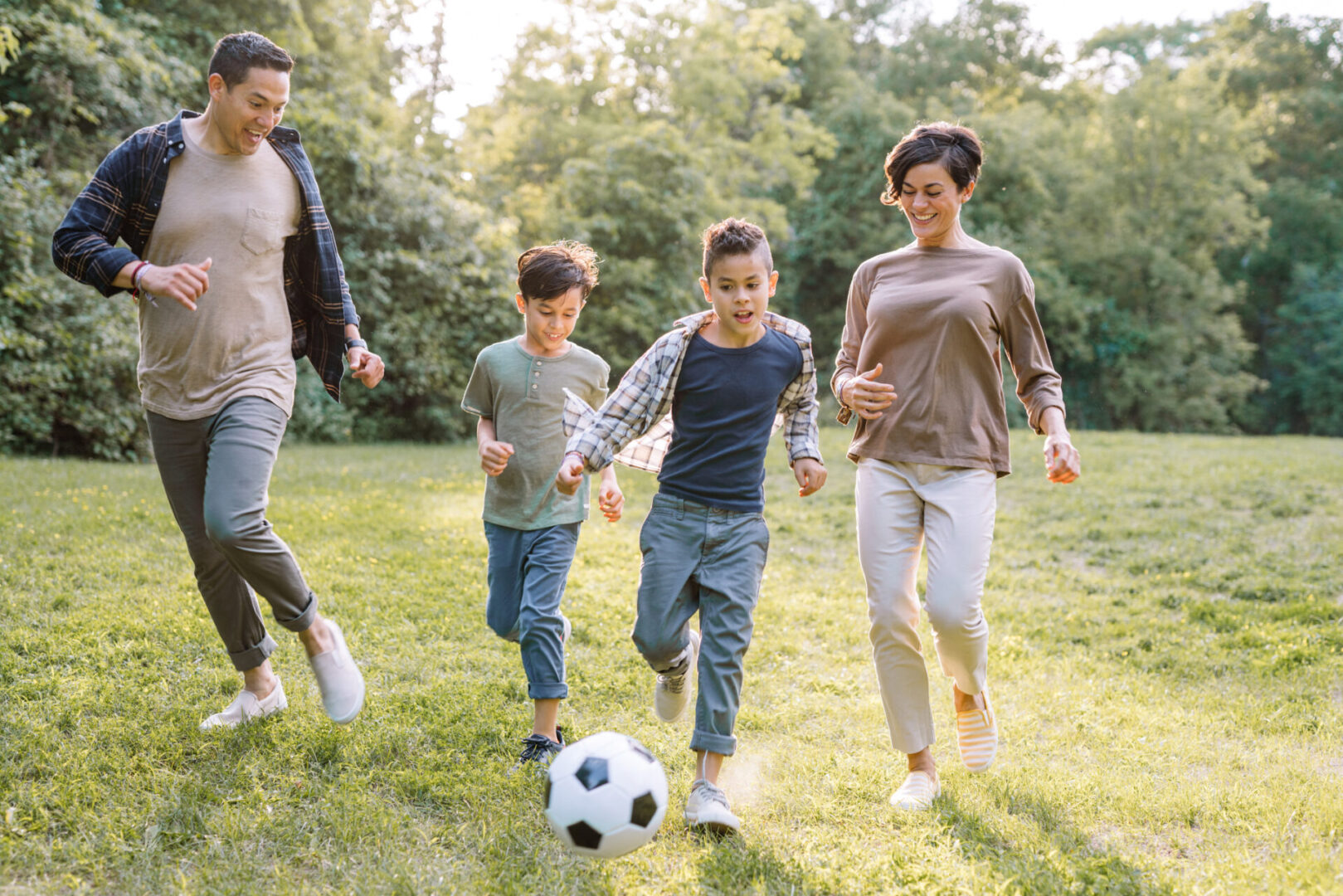 Family playing soccer in a sunny park.